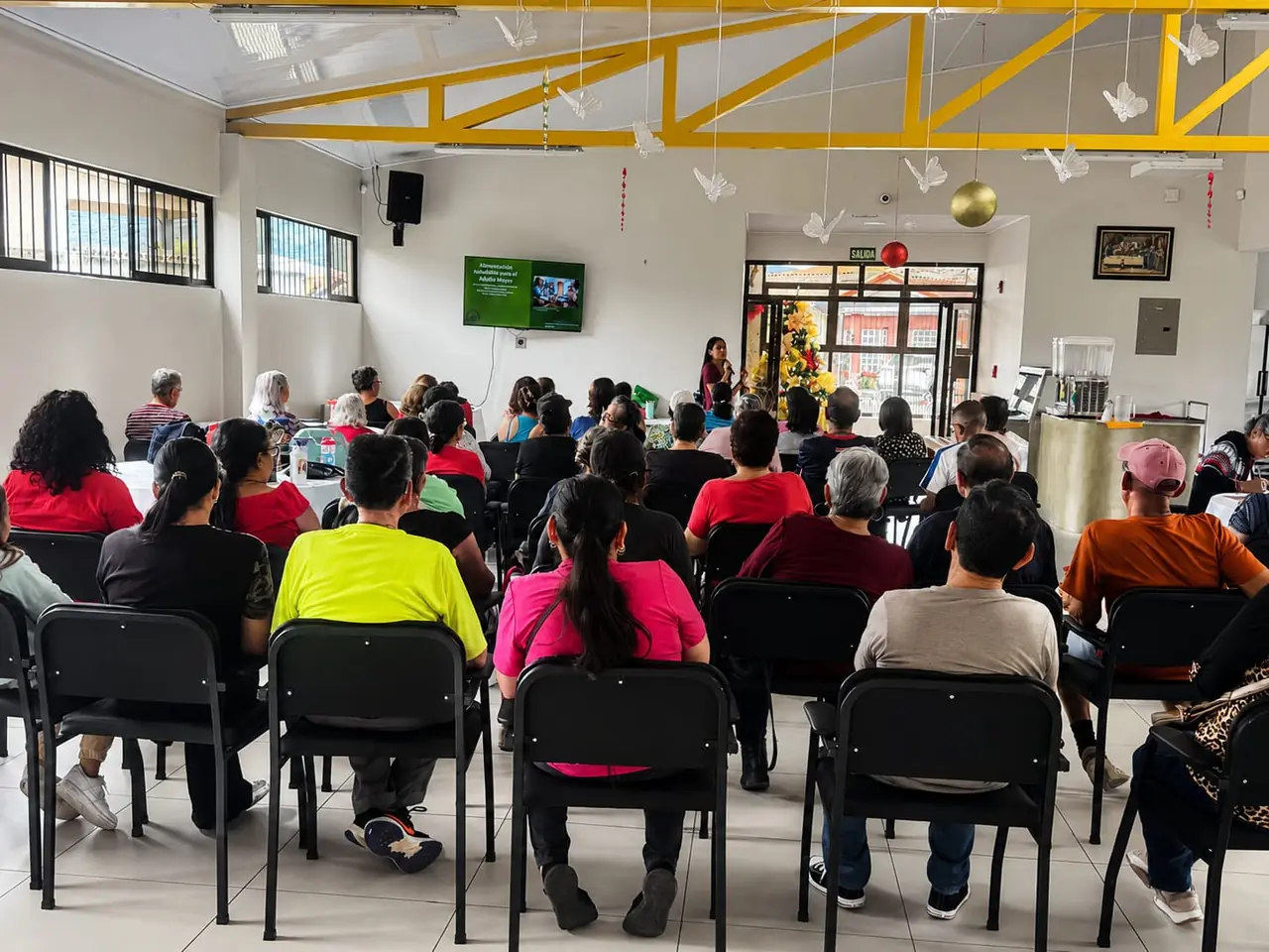 Vista desde el fondo de un salón con un grupo numeroso atento a una charla de nutrición